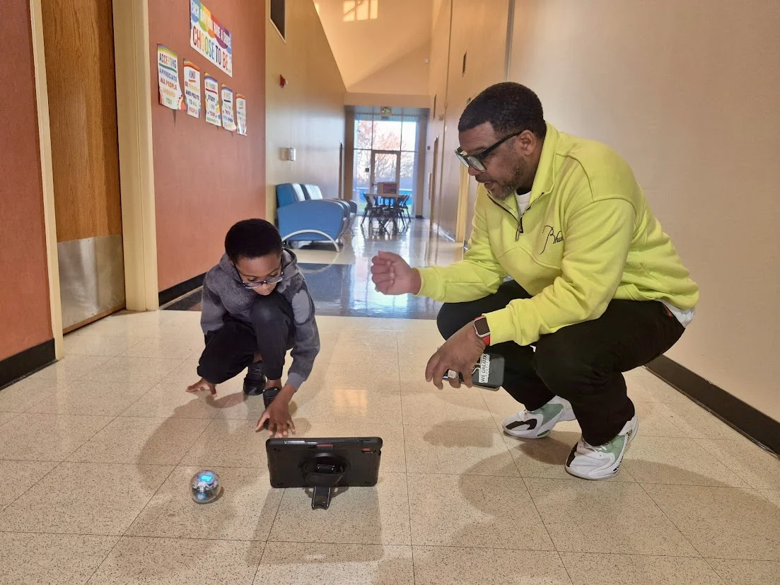 Wiley helping a young learner explore a robot in a school hallway
